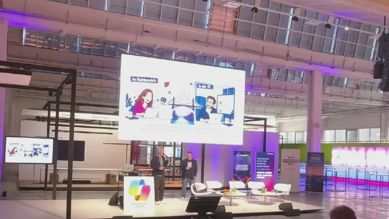 Jens Kröhnert and Thomas Gölles on stage in an industrial event hall lit in purple, with a large screen showing the illustration “The connection makes the difference”: a business user with Copilot on the left, an IT architect with a data platform on the right, and a bridge between them.